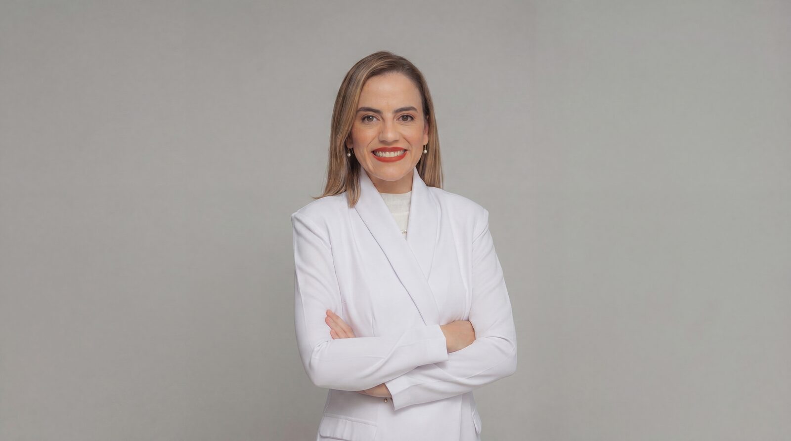 Dra. Vanessa Amoroso de jaleco branco, braços cruzados, sorrindo — retrato profissional